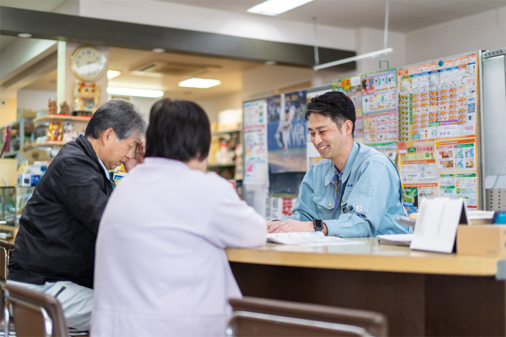 作業服姿の男性が二人の顧客とカウンター越しに相談している